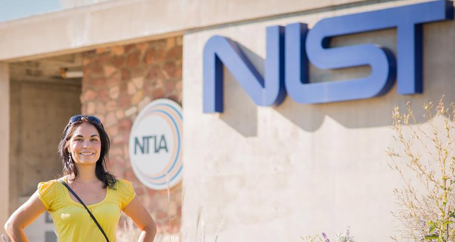 Tara Fortier in front of the NIST building with the sign behind her