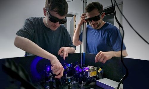 An image of Cameron, left, with intern Remy Grasland, aligning a new photon-pair source that will test new cameras