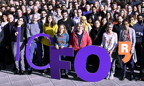 An outdoor picture of a large group of people, holding up the letters "ICFO". 