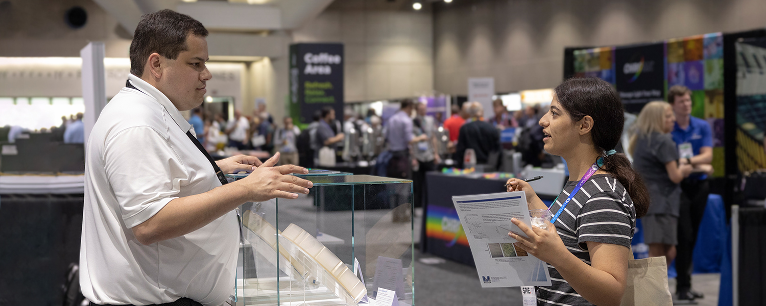 Female talks to male from an exhibitor booth at SPIE Photomask Technology + EUVL