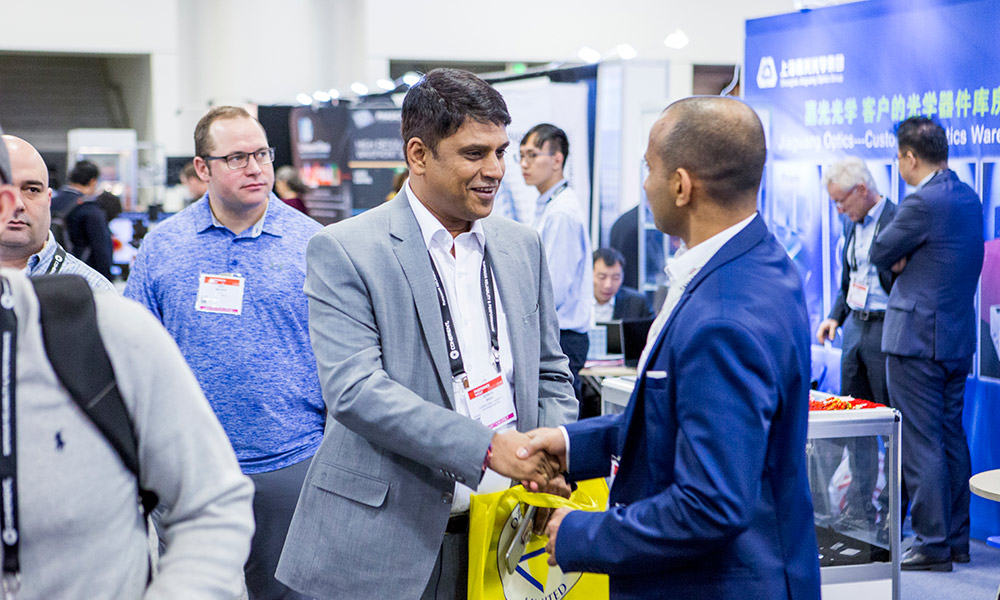 Two men shake hands while on the exhibition floor at SPIE Photonics West