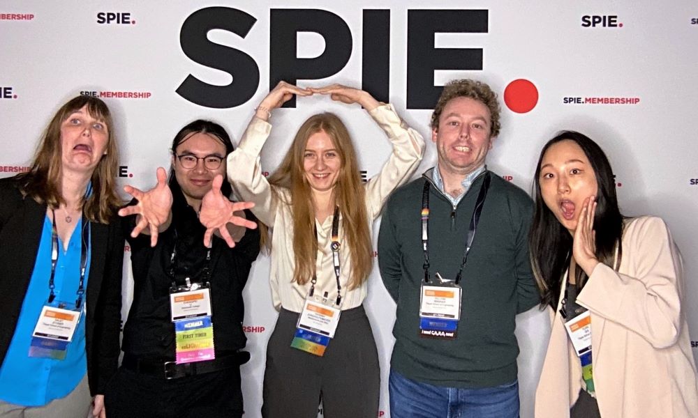 Five SPIE Student Members stand with different poses and facial expressions in front of an SPIE Membership photo booth backdrop