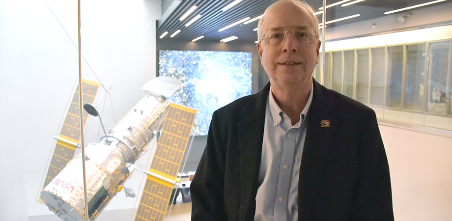 John MacKenty in the Space Telescope Science Institute's Muller Building, with a 1/5 scale model of the Hubble Space Telescope in the background.